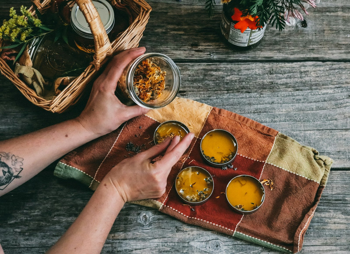 Hands filling small tins with homemade balm on a wooden table, similar to a whipped tallow balm or salve