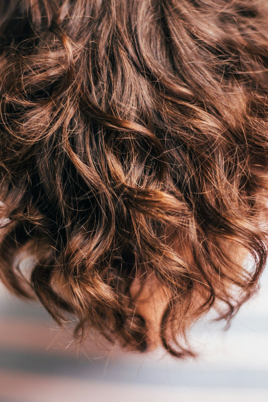 Close-up of shiny, wavy brown hair, the kind many people treat with castor oil for hair