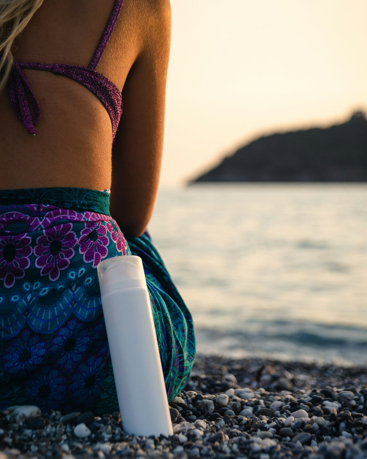 A plain white bottle of sun lotion on a pebble beach beside the sea