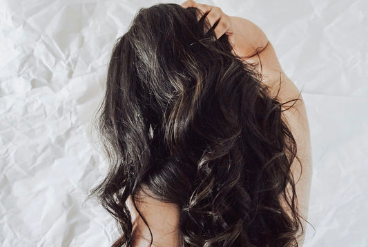 The back of a woman's head with long, soft, glossy dark wavy hair, the kind of shine Davines OI shampoo is designed for