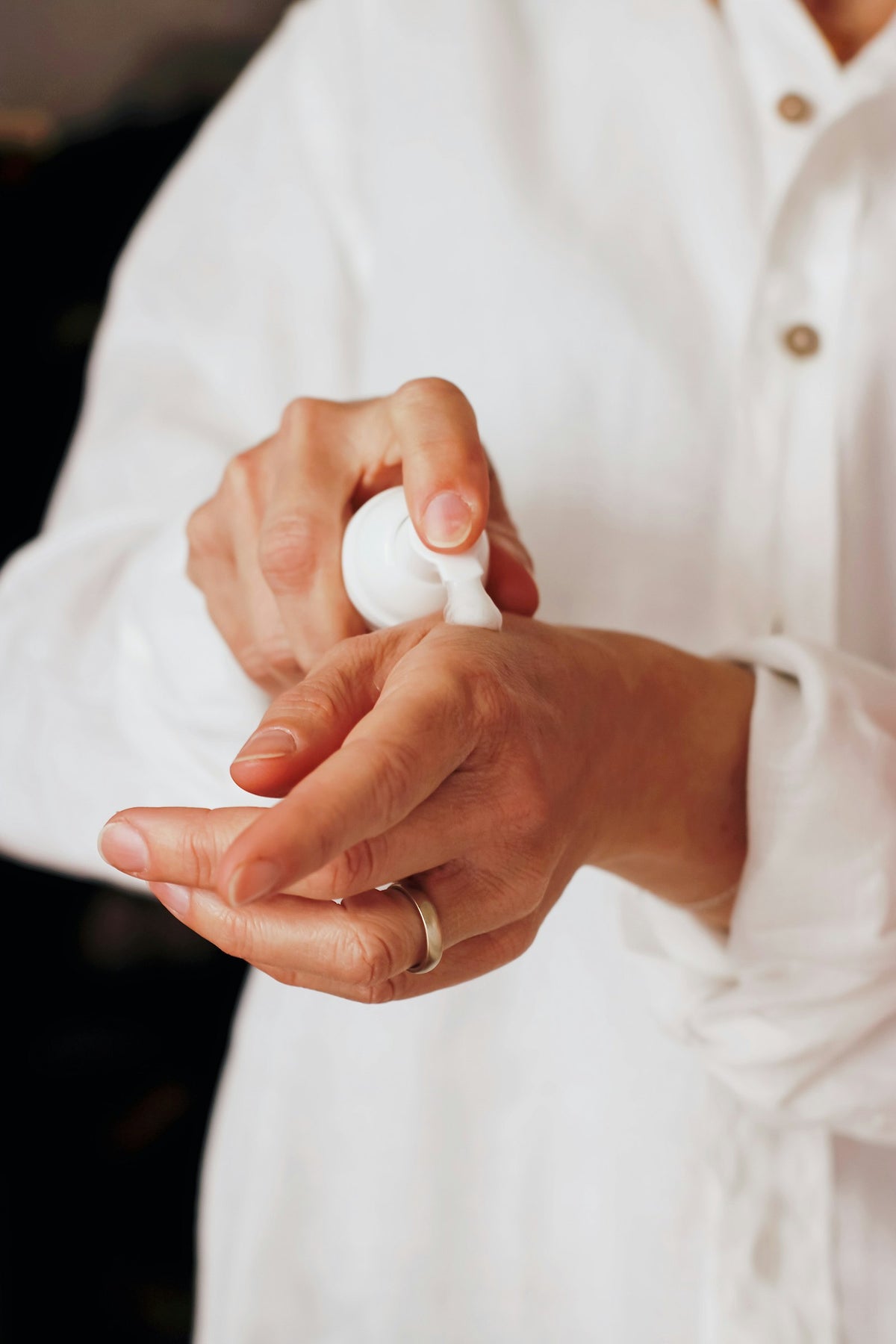 Hands dispensing lotion from a white pump bottle