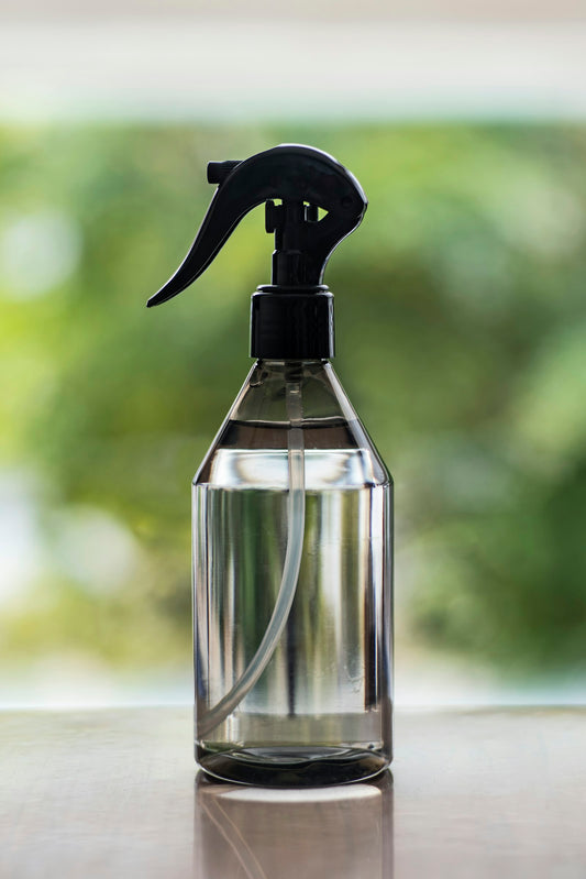 A clear spray bottle with a black trigger on a table by a window, similar to a magnesium spray bottle