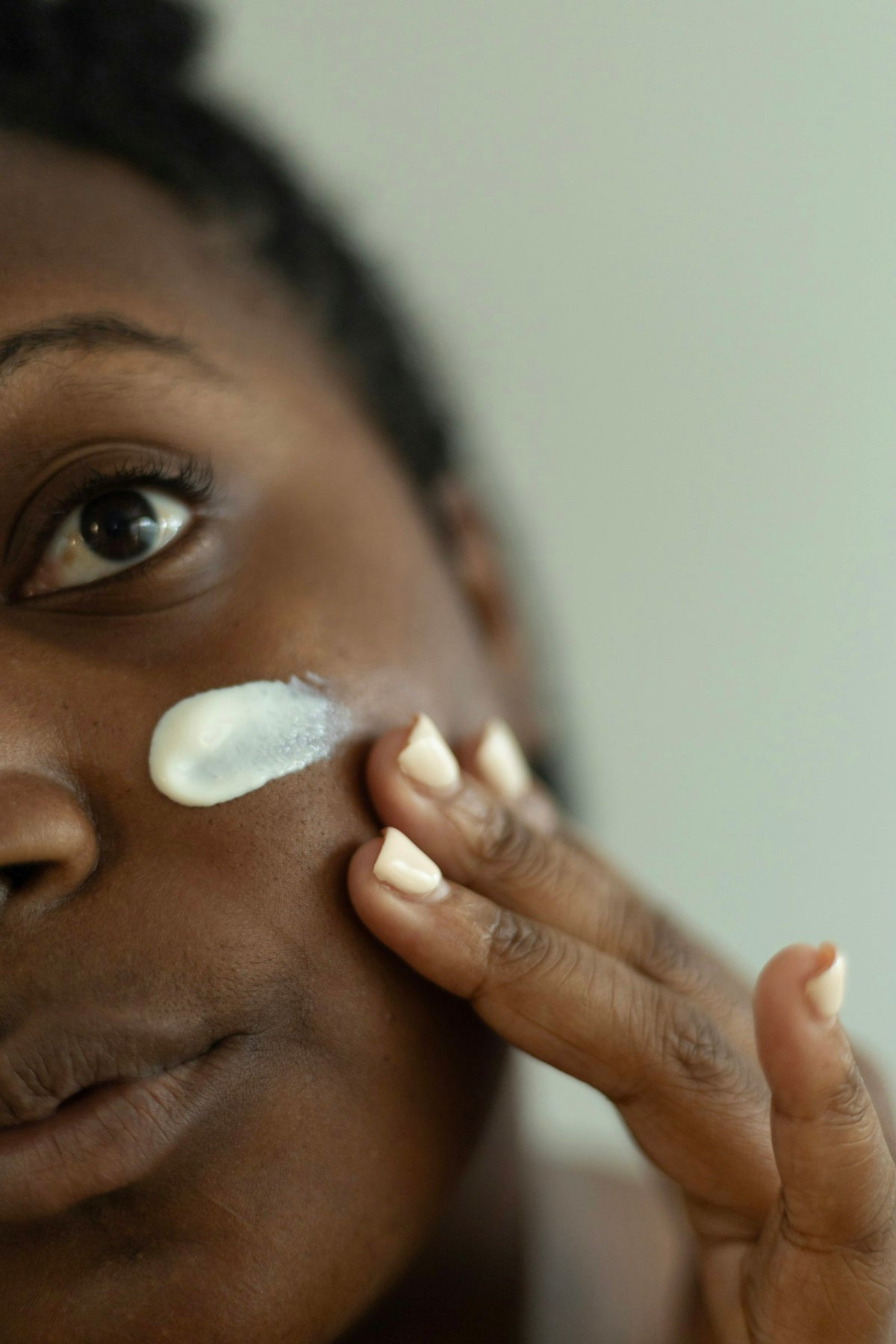 Woman with a dab of white moisturizer on her cheek, smoothing it in with her fingertips