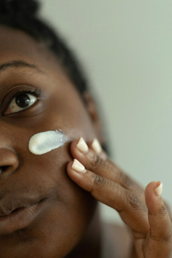 Woman with a dab of white moisturizer on her cheek, smoothing it in with her fingertips
