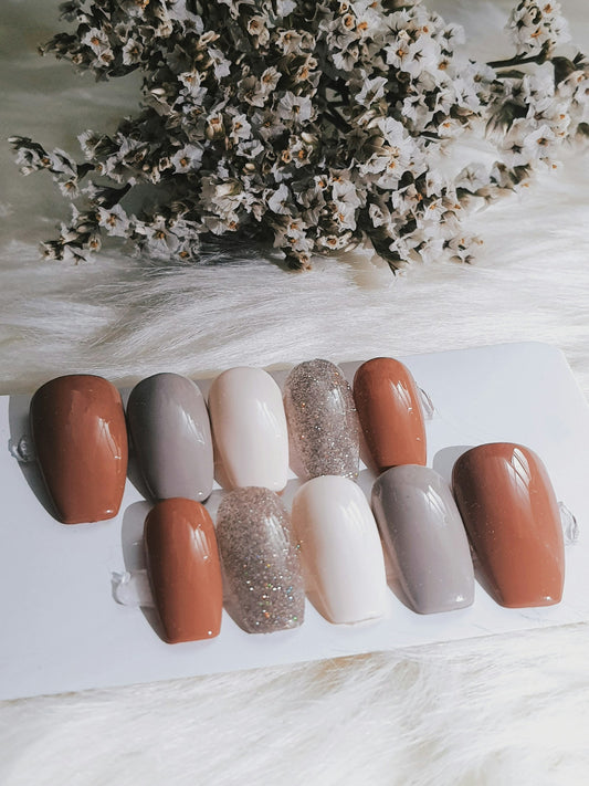 Press-on nails in neutral shades of brown, gray, white and glitter on a soft white surface