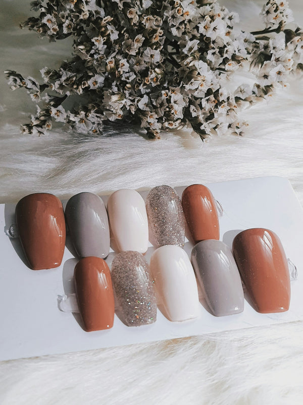 Press-on nails in neutral shades of brown, gray, white and glitter on a soft white surface