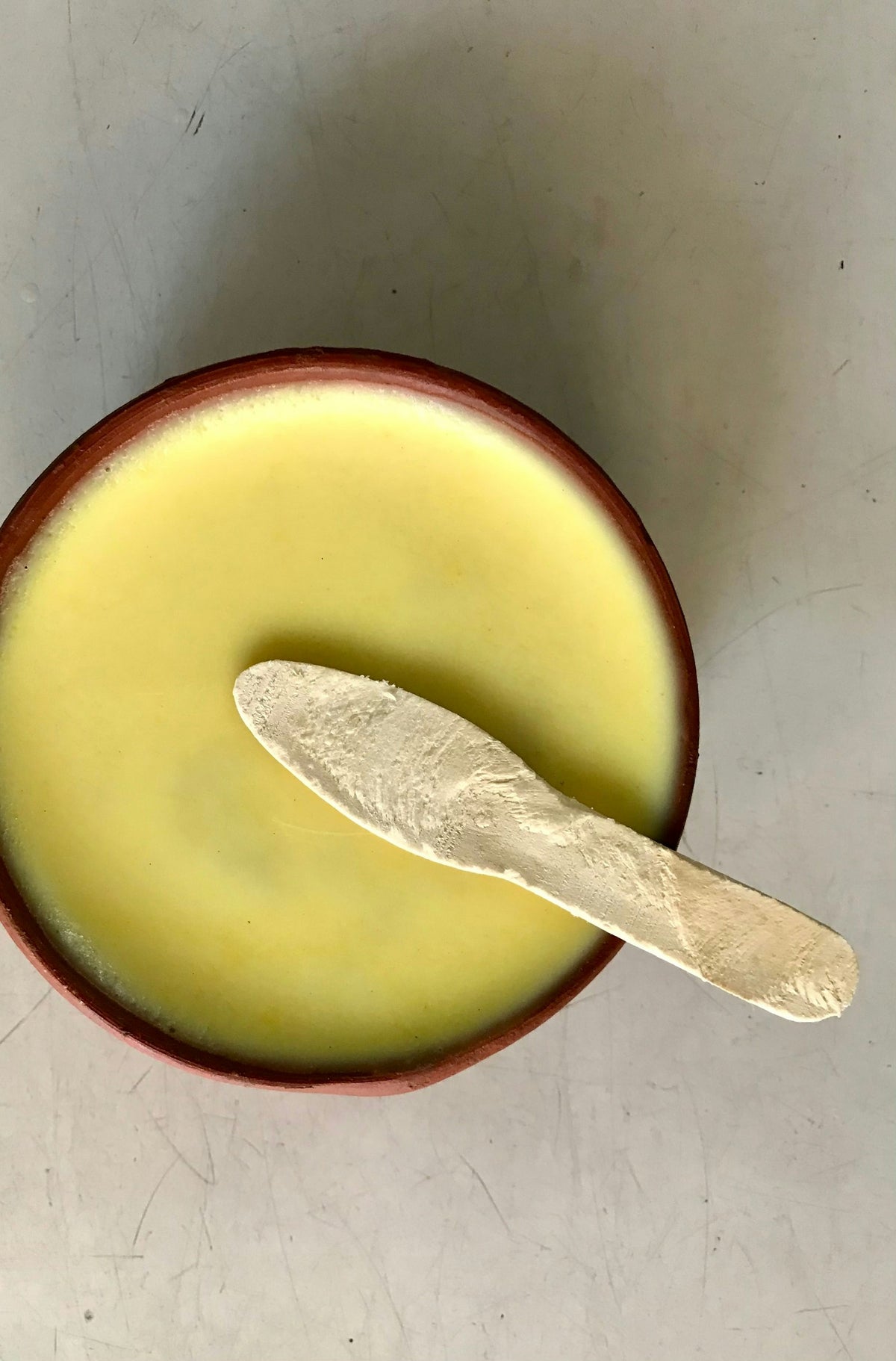 A clay bowl of pale yellow balm with a spreader, the kind of rich texture beef tallow for skin is known for