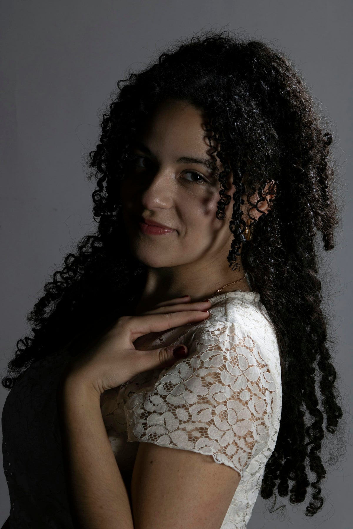 A smiling woman with long, defined curly hair against a gray background, the result of a curly hair products routine
