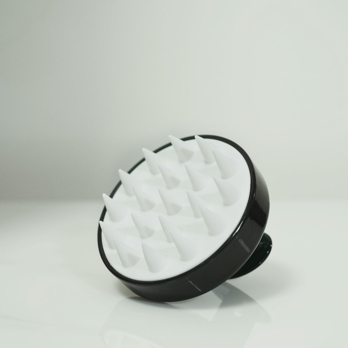 A black and white silicone scalp scrub brush with soft bristles on a pale background