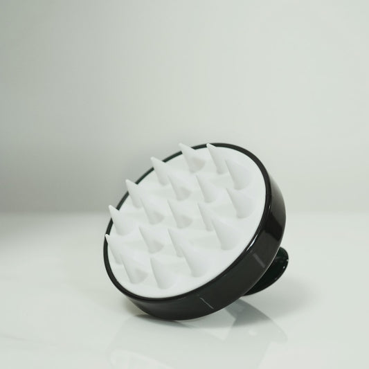 A black and white silicone scalp scrub brush with soft bristles on a pale background