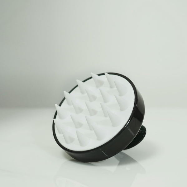 A black and white silicone scalp scrub brush with soft bristles on a pale background